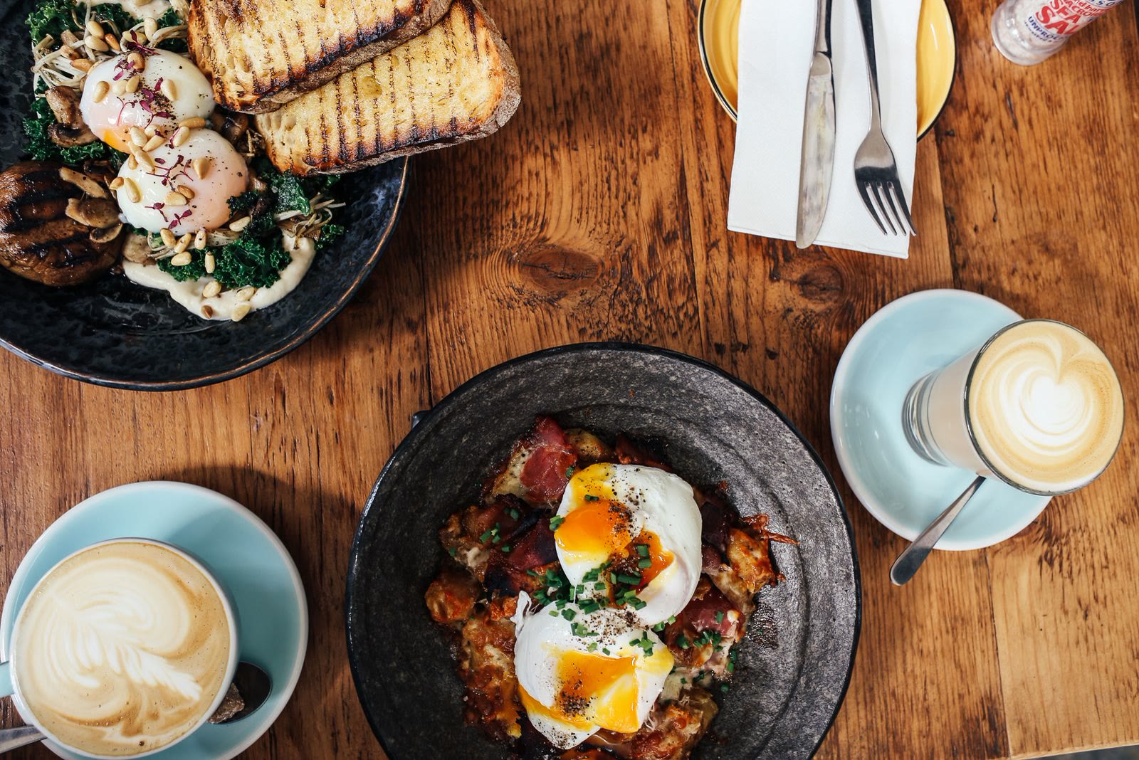 Brunch plates with eggs, toast and lattes on a wooden table
