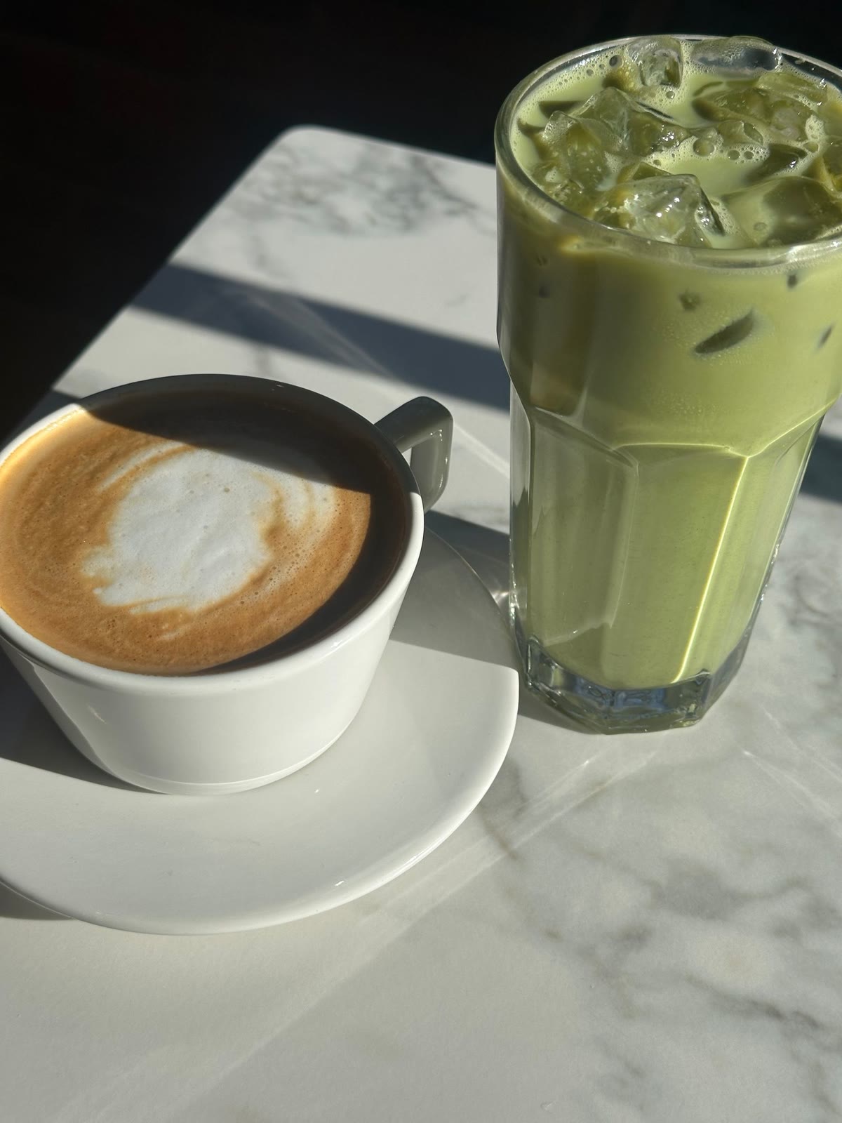 A latte and an iced matcha side by side in the sun
