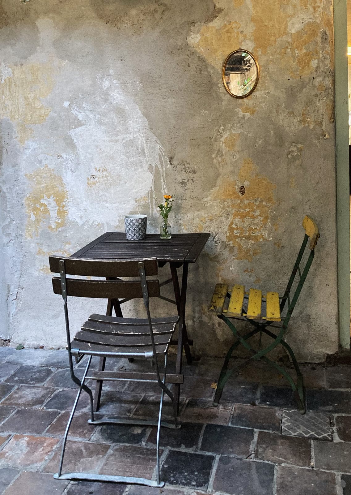 Small café table and chairs against a sunlit old wall