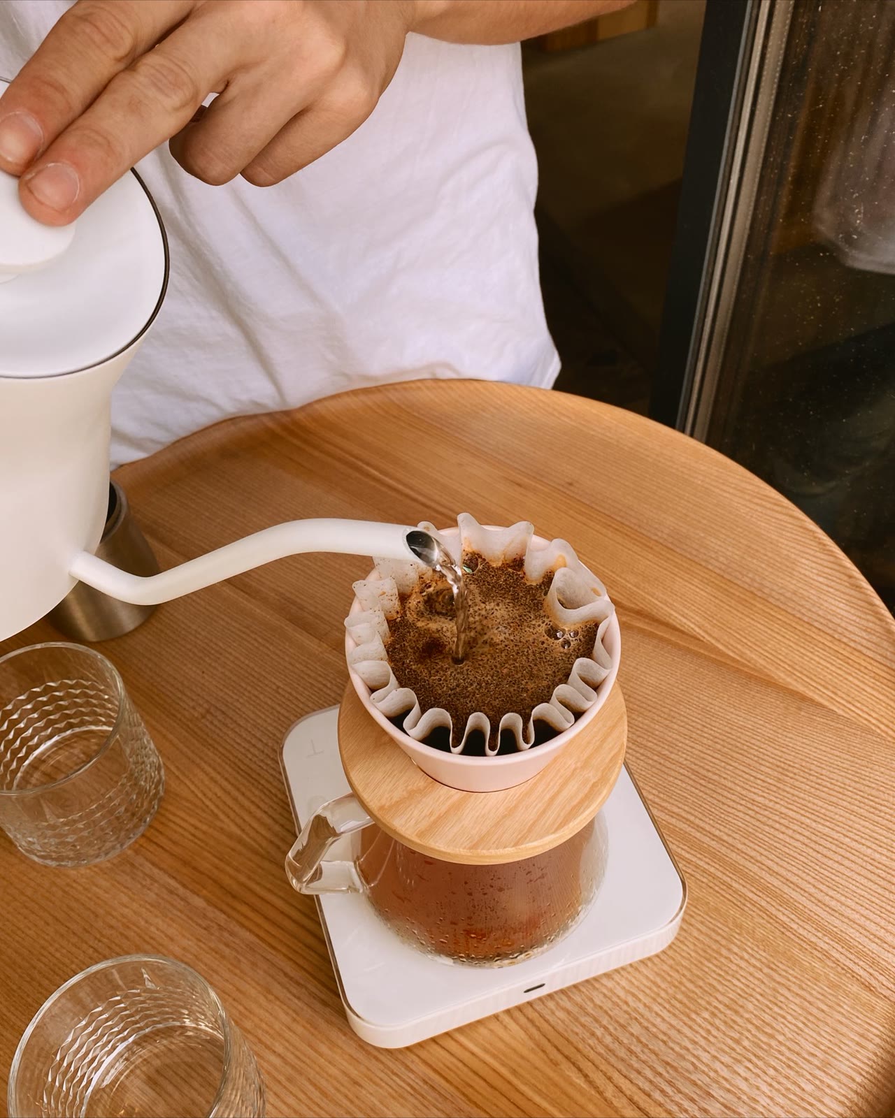 Barista pouring water over a pour-over coffee filter on a wooden table