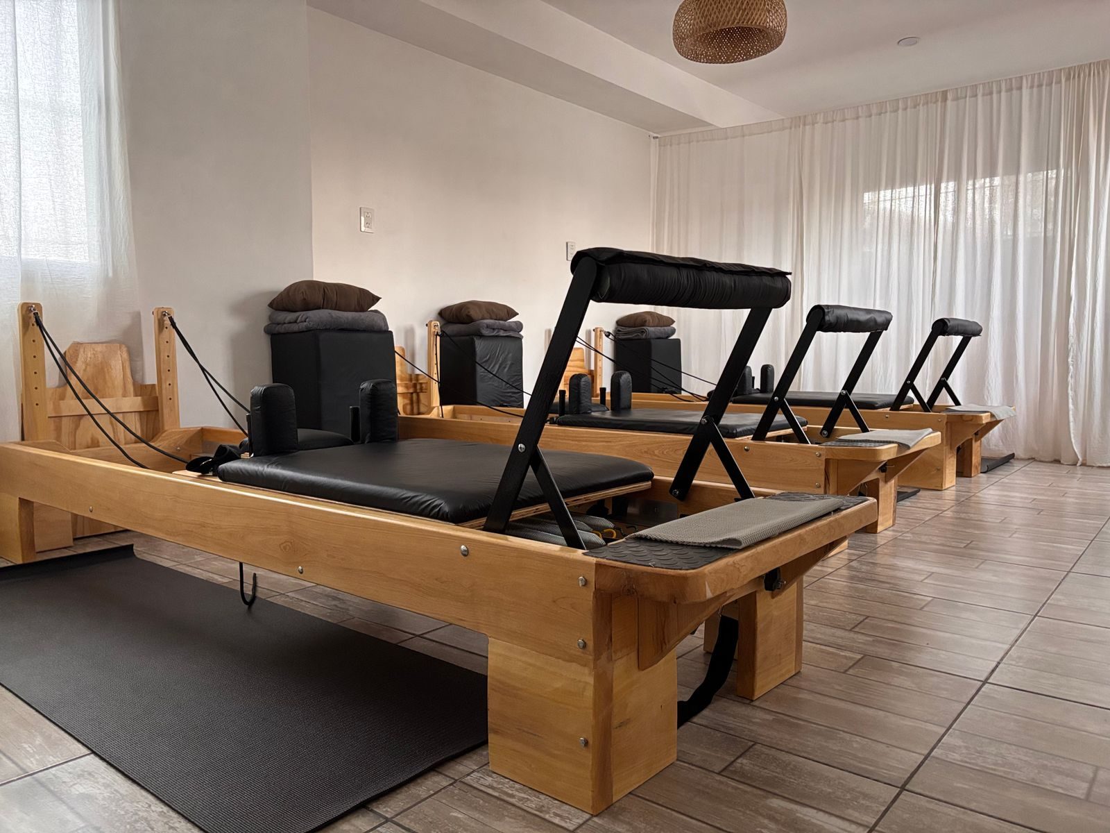 Row of wooden reformers in a calm, curtained pilates studio