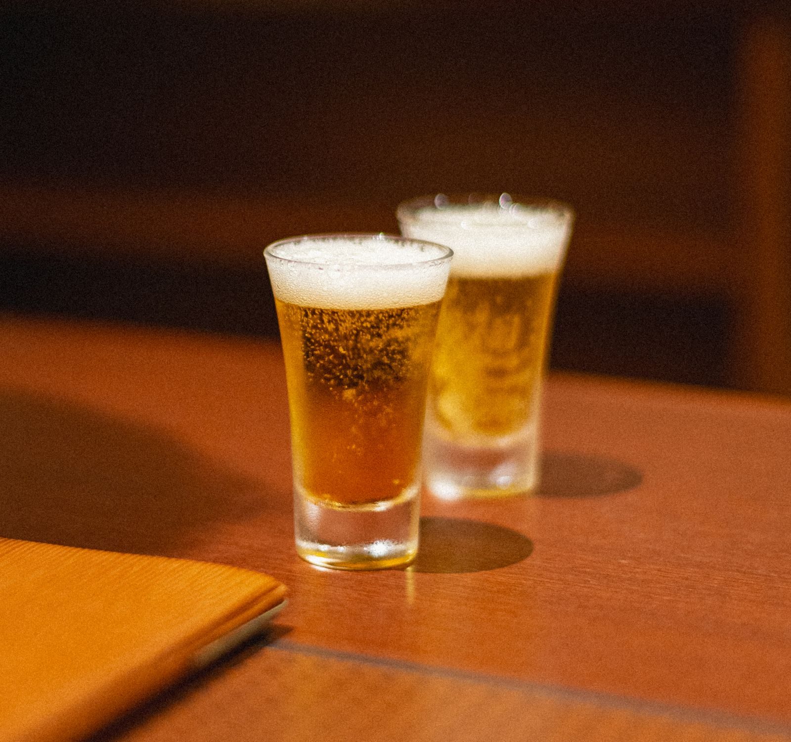 Two small glasses of cold beer on a warm wooden table
