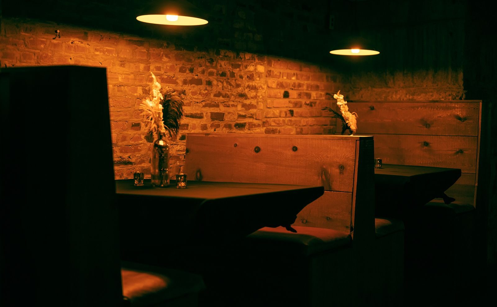 Wooden booths under low pendant lamps against a warm brick wall at night