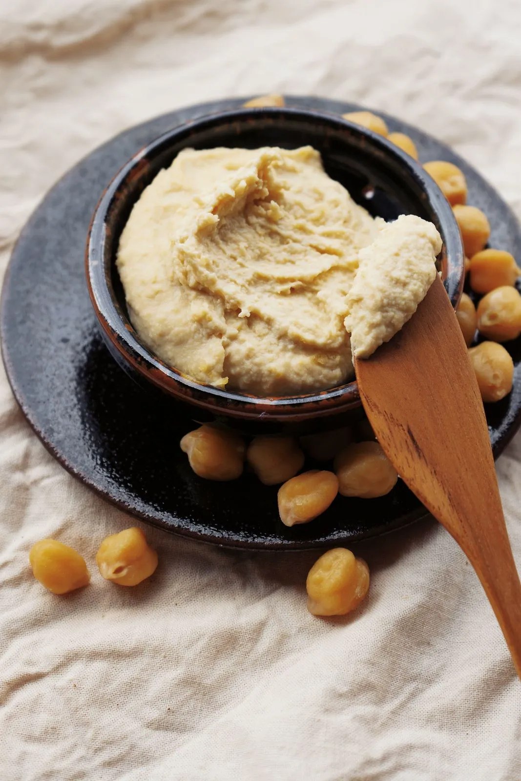 Hummus in a dark bowl with chickpeas and a wooden spoon