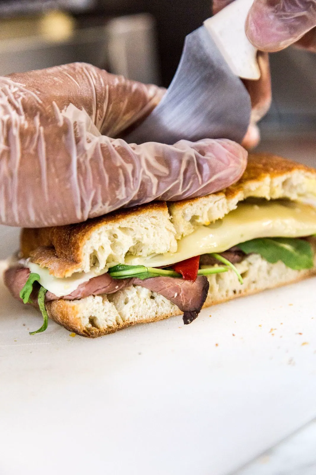 Gloved hands cutting a focaccia sandwich
