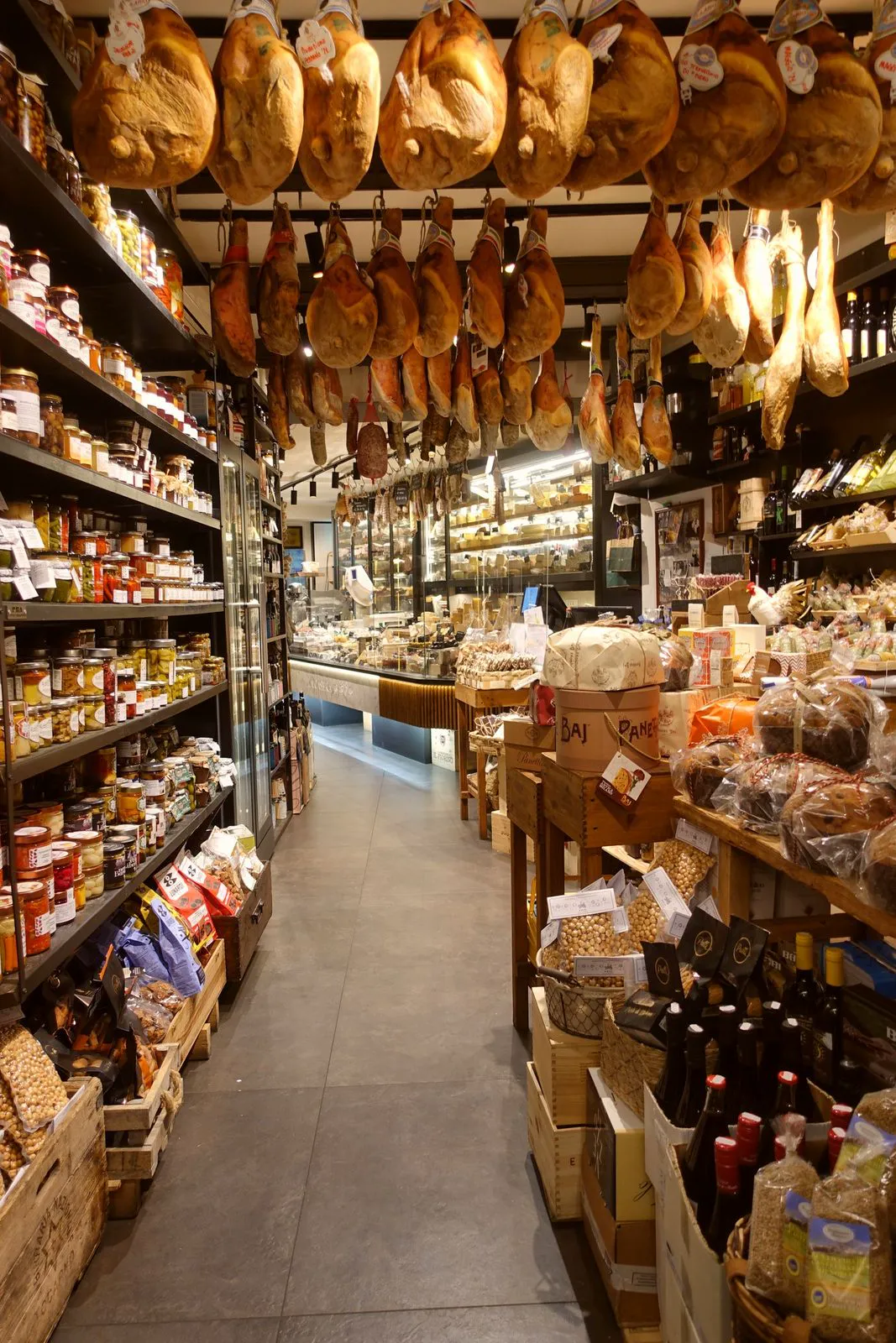 Narrow deli aisle lined with jars, bottles and hanging hams