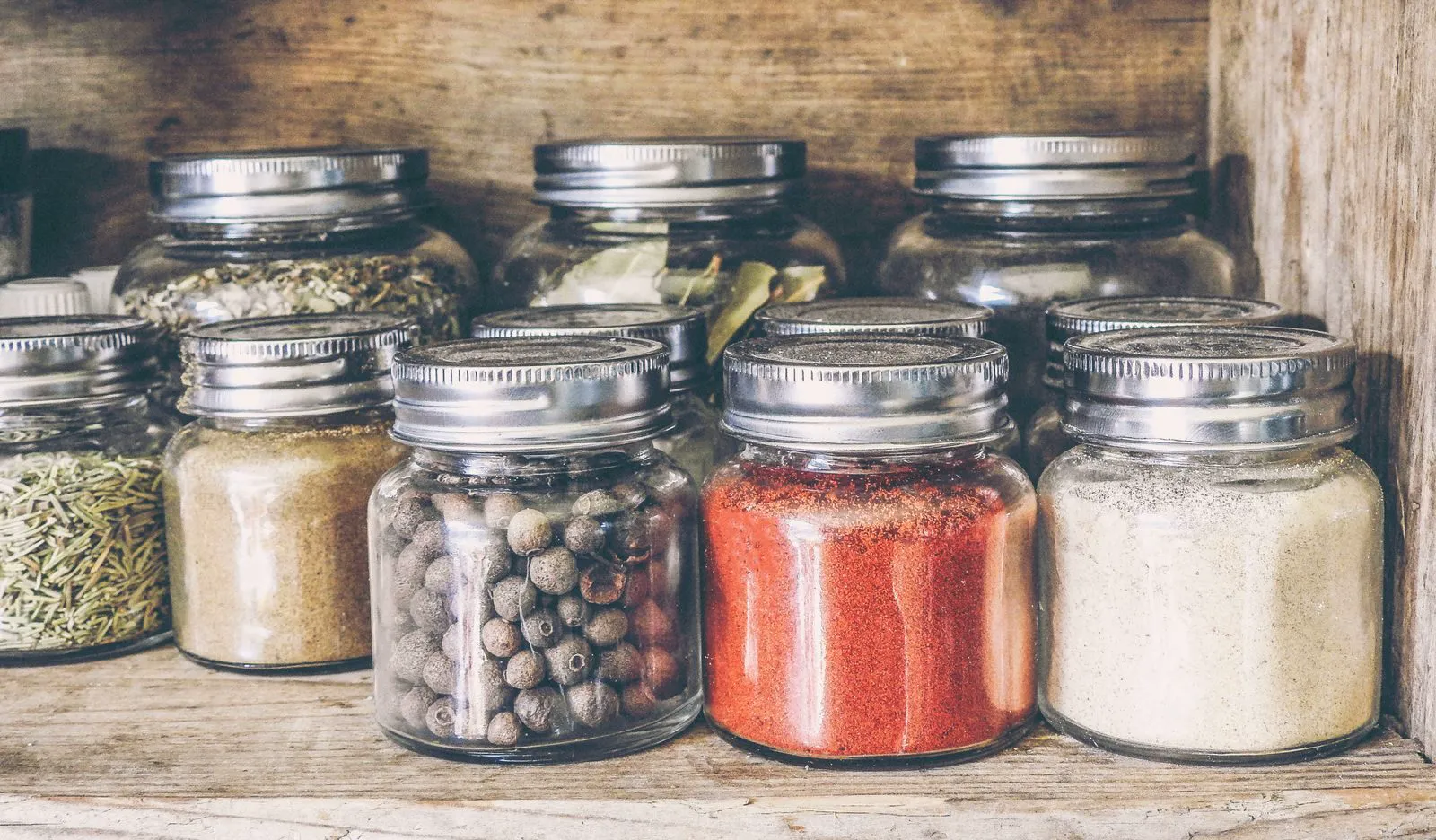 Glass jars of spices on a rustic wooden shelf