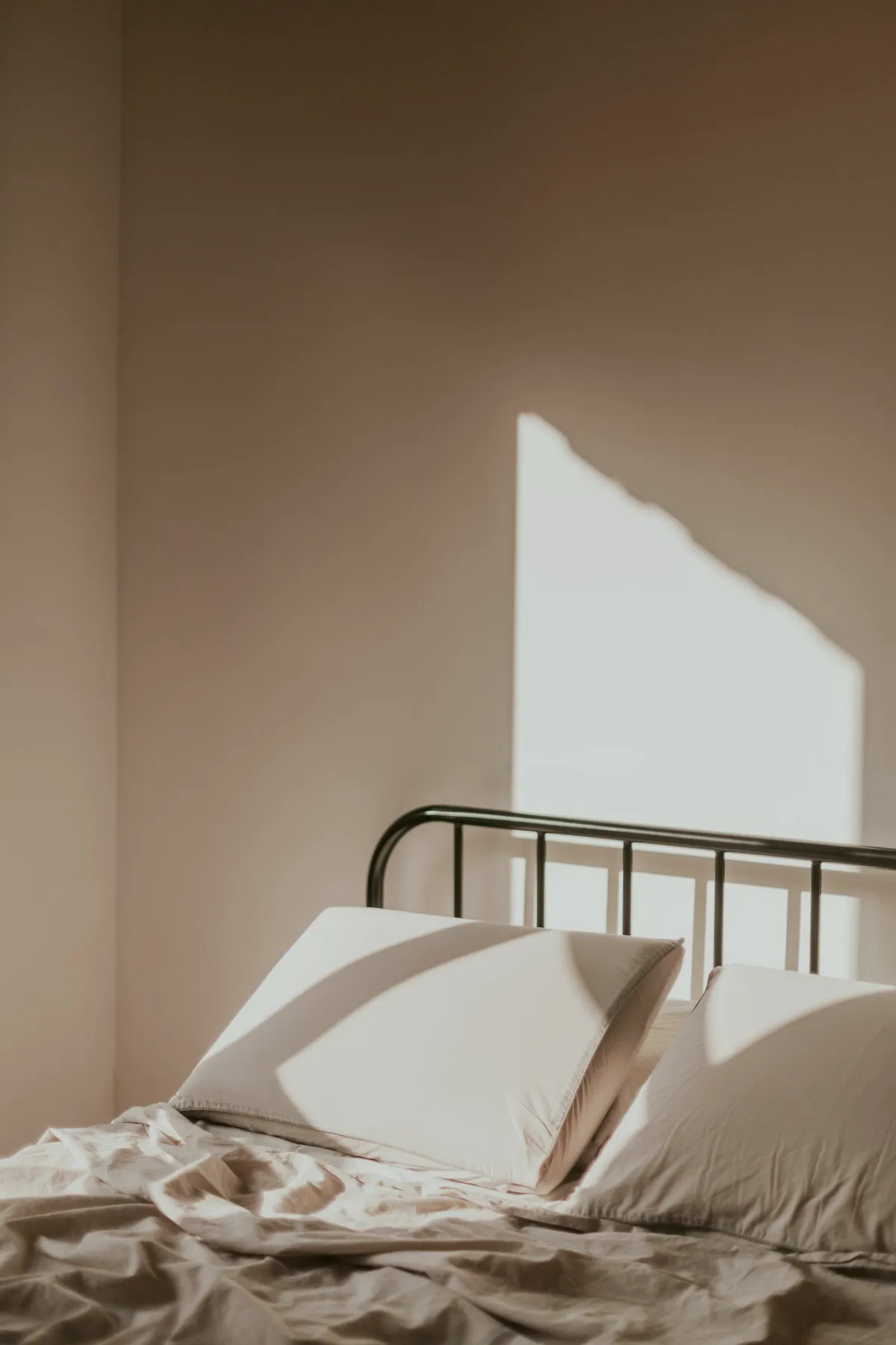 Iron bed against a clay coloured wall with a patch of sun