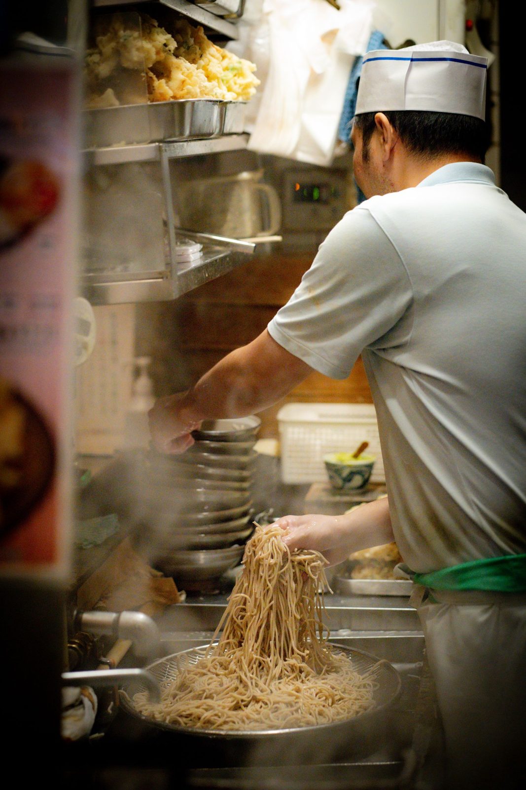Cook lifting fresh noodles from a steaming pot