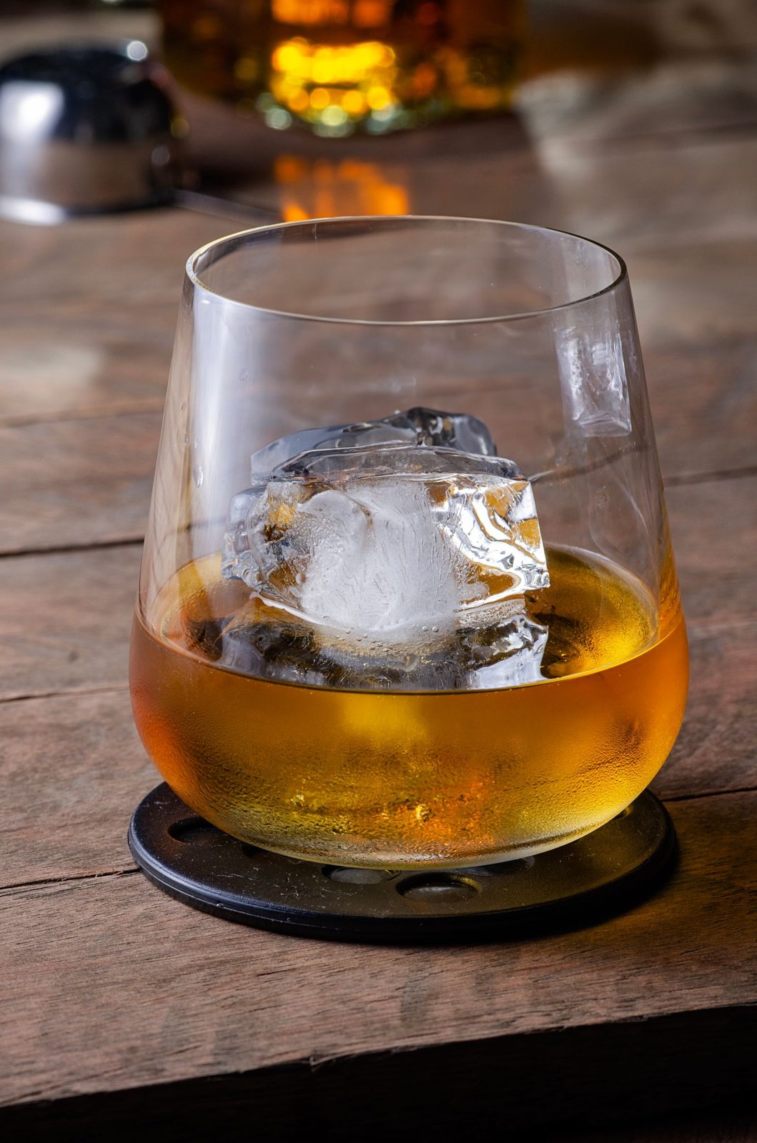 Whisky over a large ice cube on a wooden bar