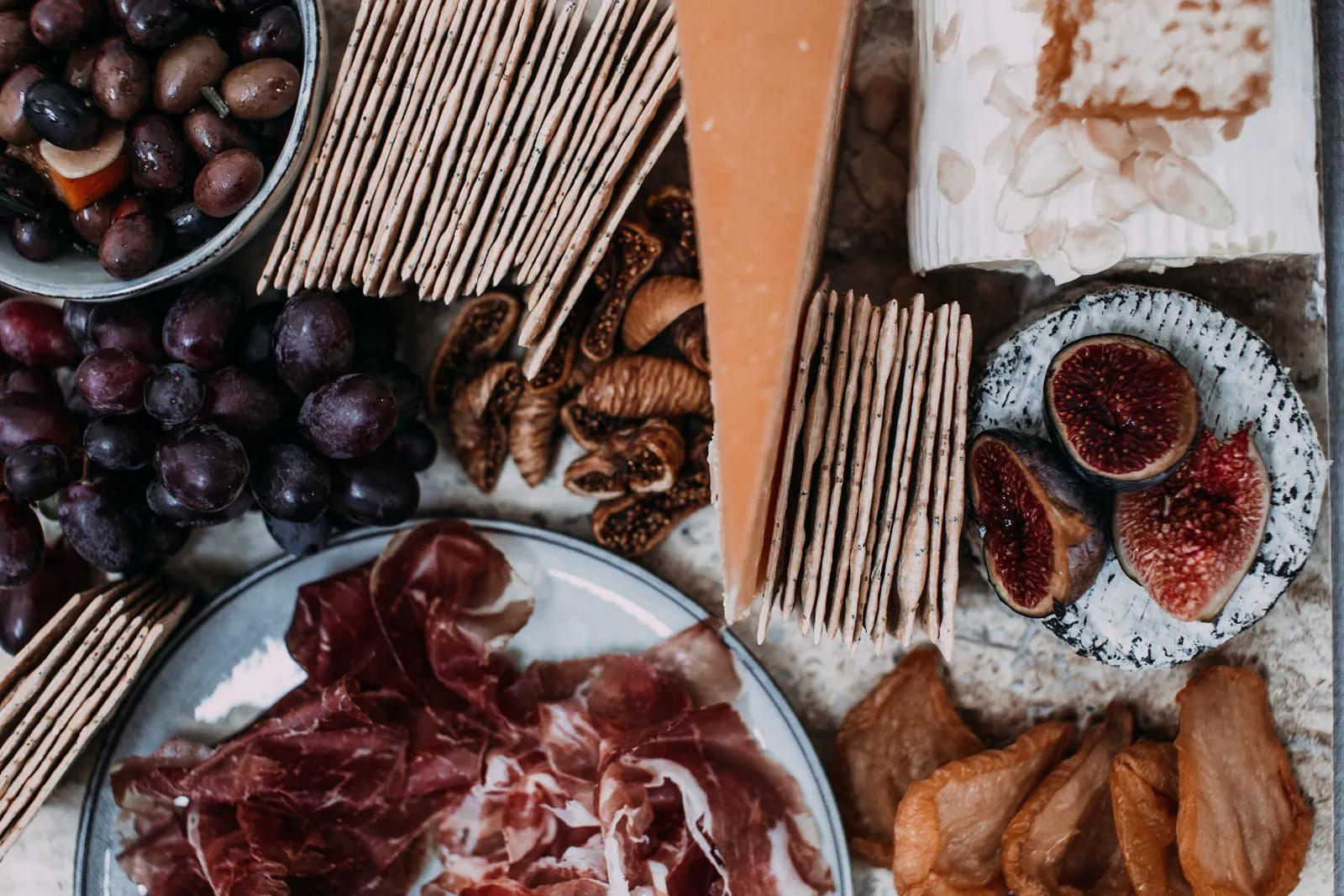 Board with prosciutto, figs, olives, grapes and crackers