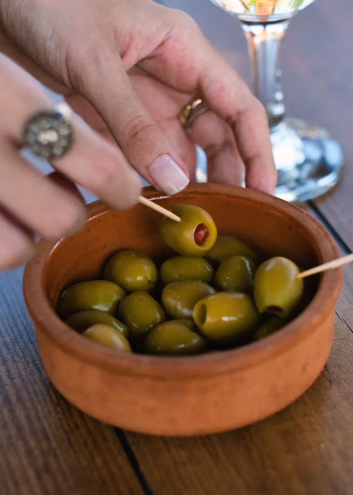 Hands picking a green olive from a terracotta bowl with a toothpick