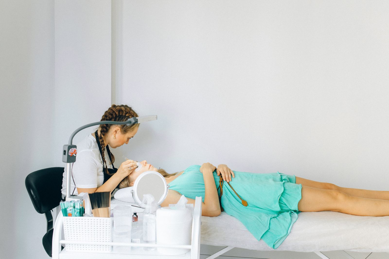 An artist working on a client's brows in a bright white studio