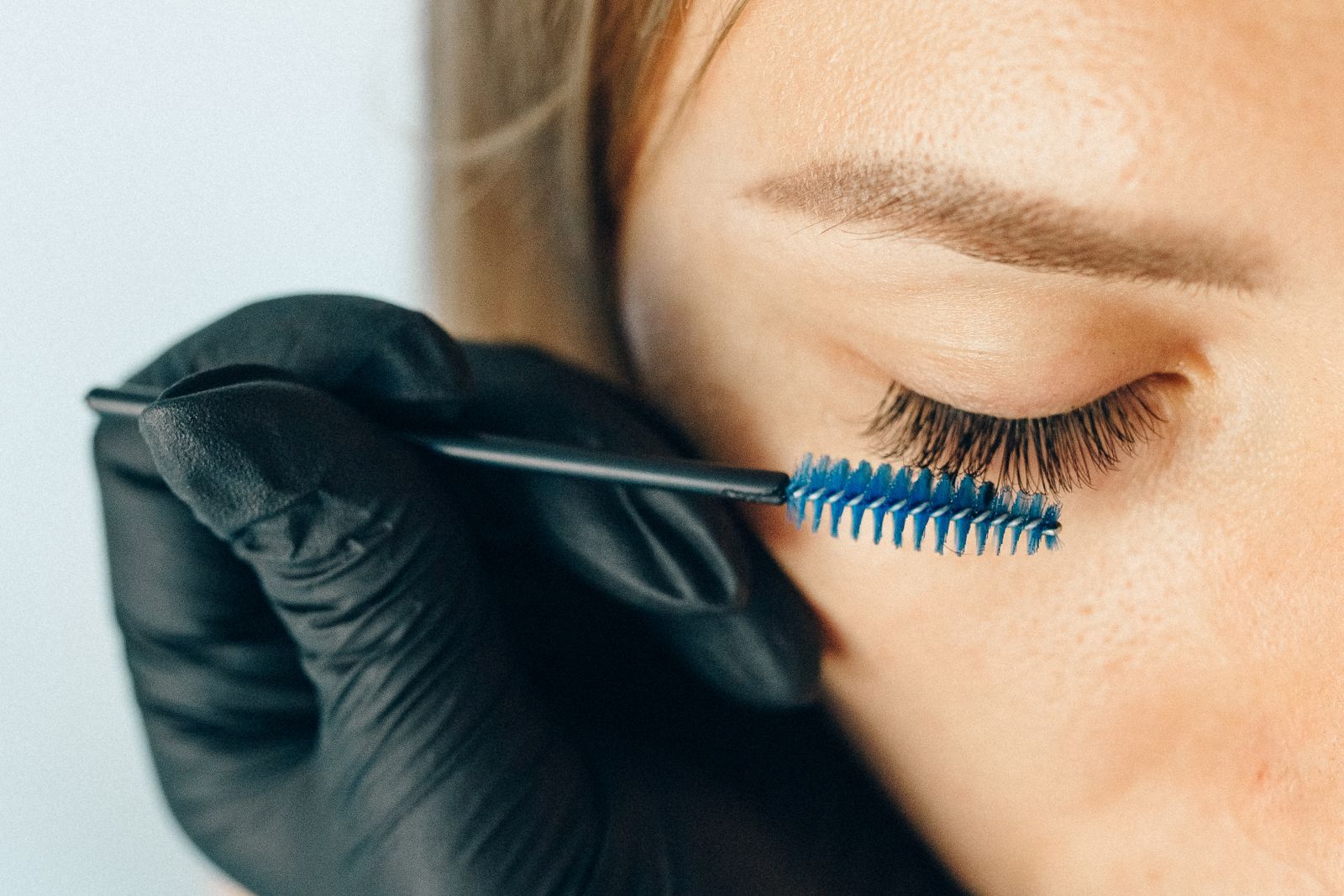 A gloved hand combing lashes with a spoolie