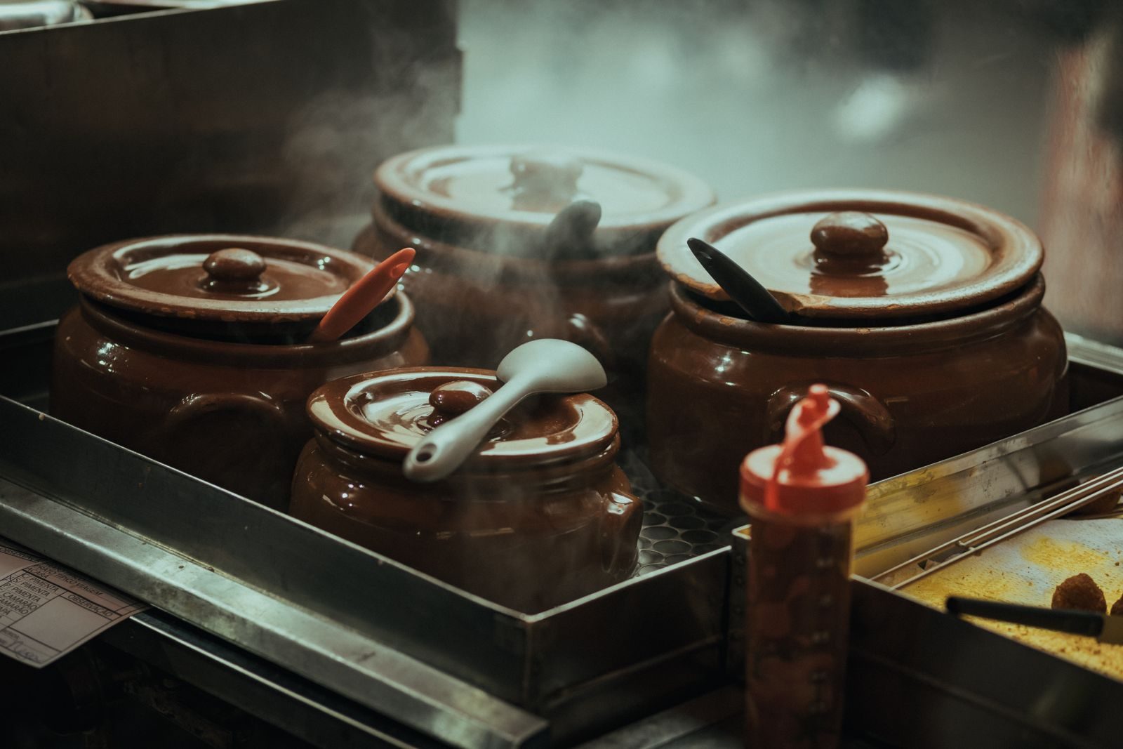 Steam rising from clay pots of broth on a kitchen stove