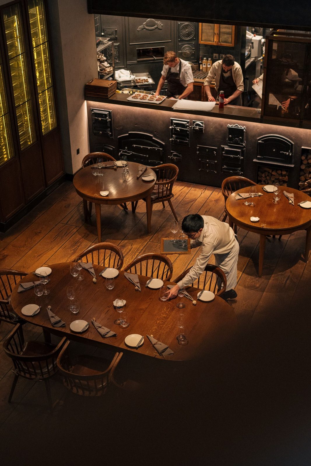 Warm dining room with wooden tables being set before service